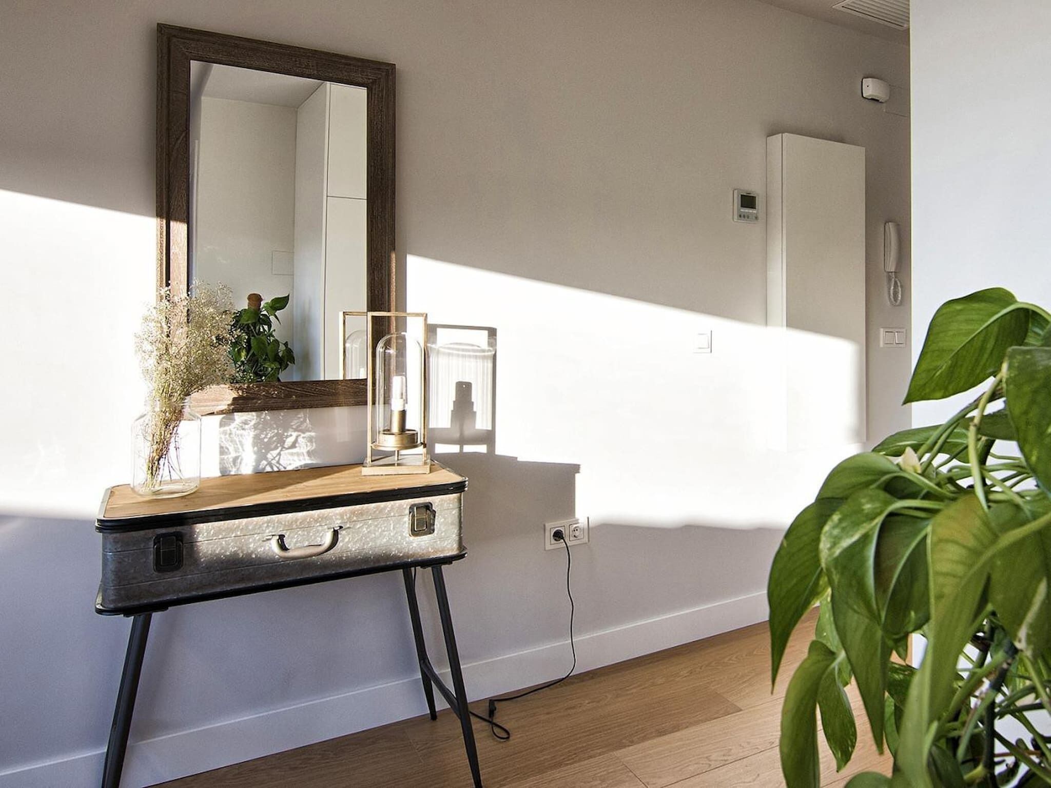A room with a wooden dresser, a mirror, a potted plant, and a wall-mounted thermostat.