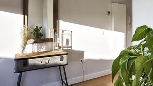 A room with a wooden dresser, a mirror, a potted plant, and a wall-mounted thermostat.