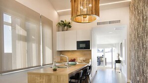 A modern kitchen with a wooden island, black bar stools, a built-in microwave, and a pendant light.