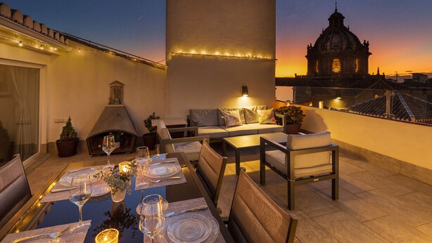 An outdoor dining area with a table set for six, a fireplace, and a view of a historic building at sunset.