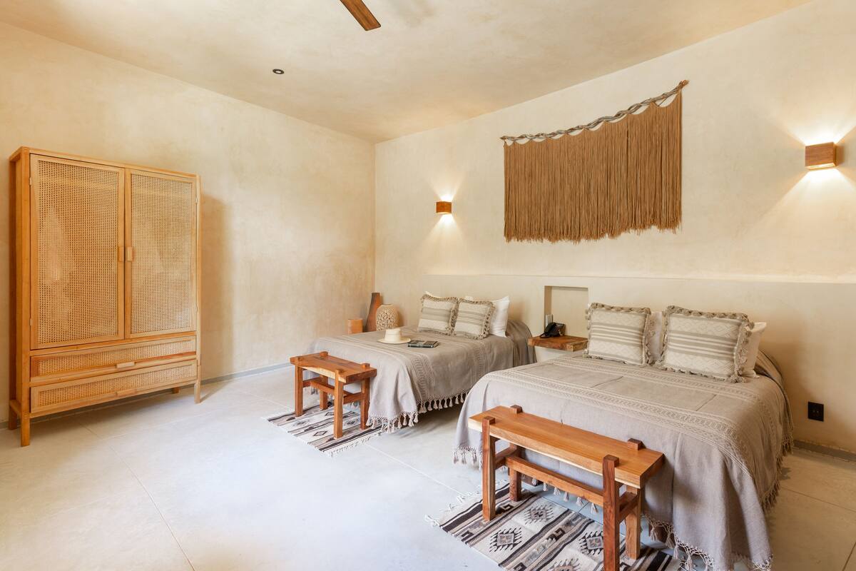 Un dormitorio con dos camas, un armario de madera y un tapiz tejido en la pared.