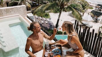 Um casal jantando perto de uma piscina, com vista para a praia e palmeiras.