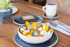 A breakfast setting with a bowl of fruit salad, a slice of bread, and a cup of coffee on a wooden table. - Hotel Ma'xanab (Tulum)