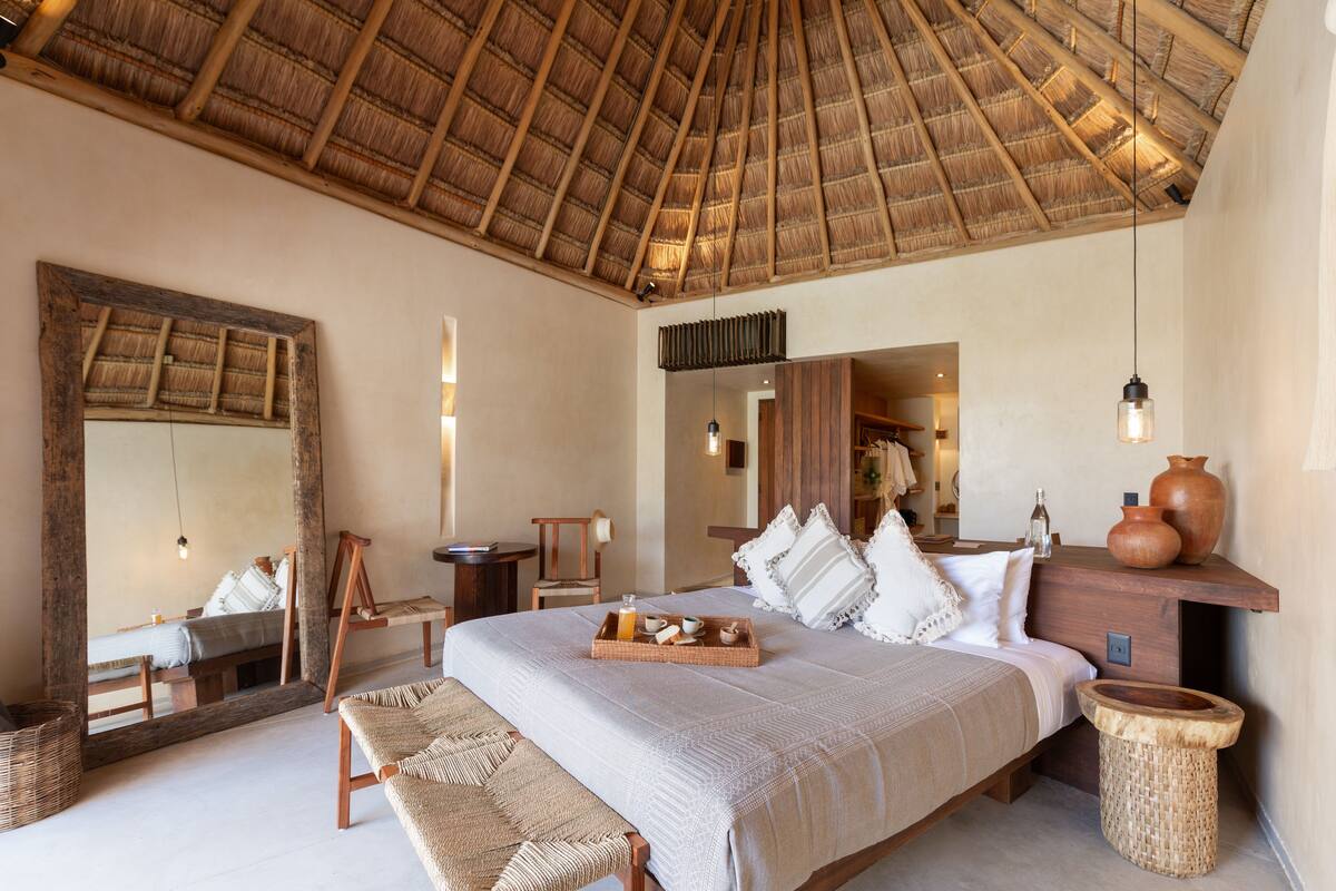 Un dormitorio amplio con una cama grande, un banco de madera, un espejo y un techo rústico.
