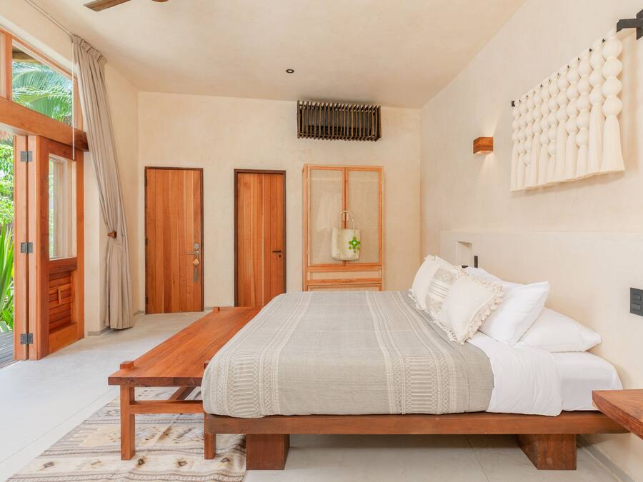 Une chambre à coucher avec un lit en bois, une table de chevet en bois, une grande fenêtre avec des rideaux et une porte.
