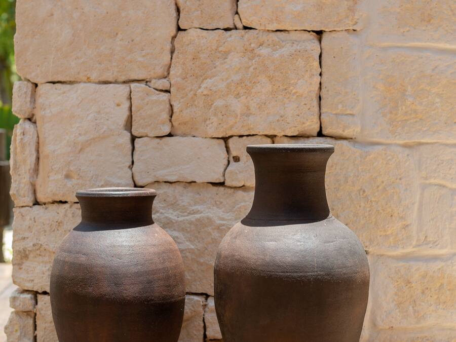 Dos jarrones de cerámica rústica sobre una mesa de madera frente a una pared de piedra.