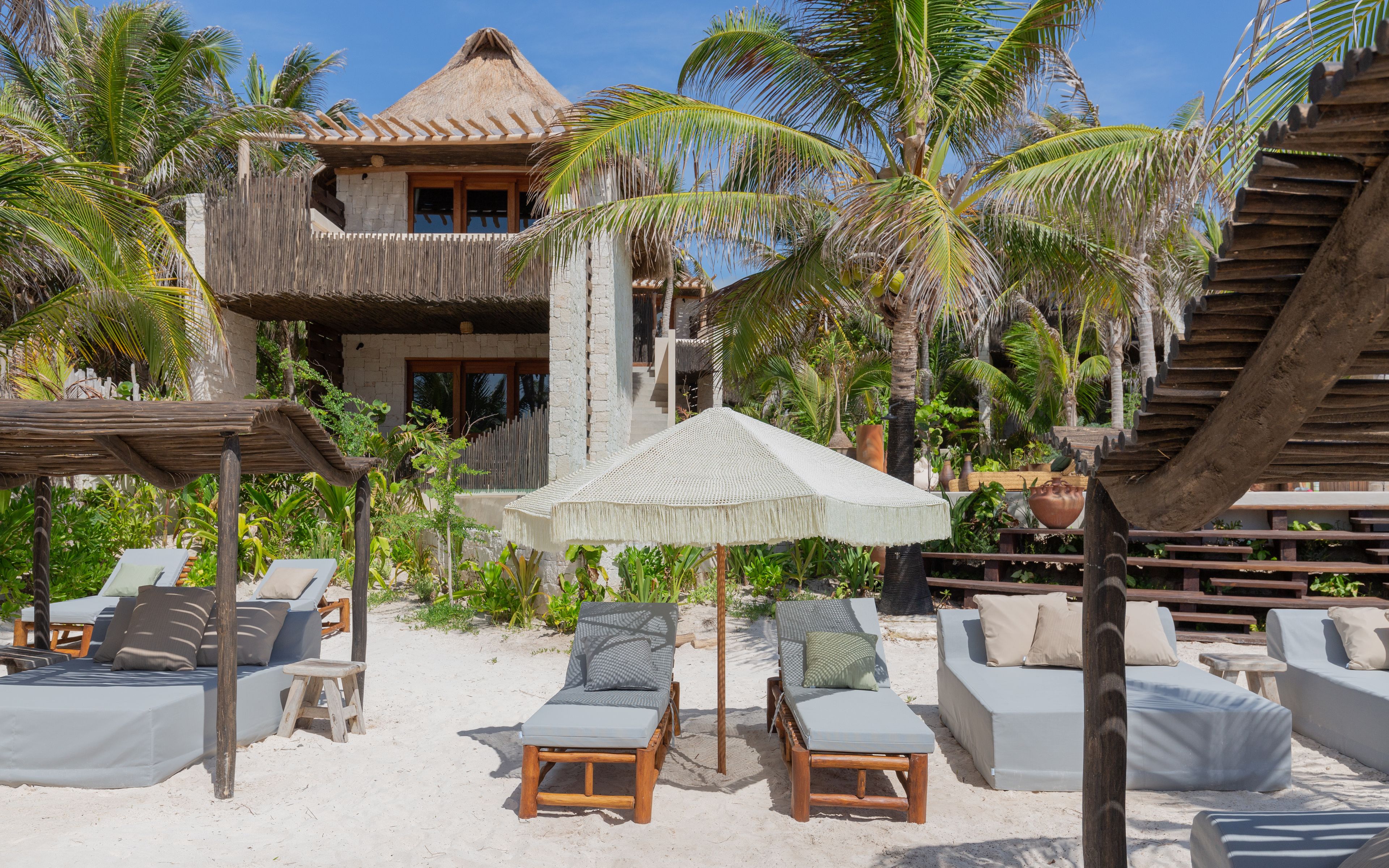A beachfront property with a thatched-roof building, lounge chairs, and a covered seating area.