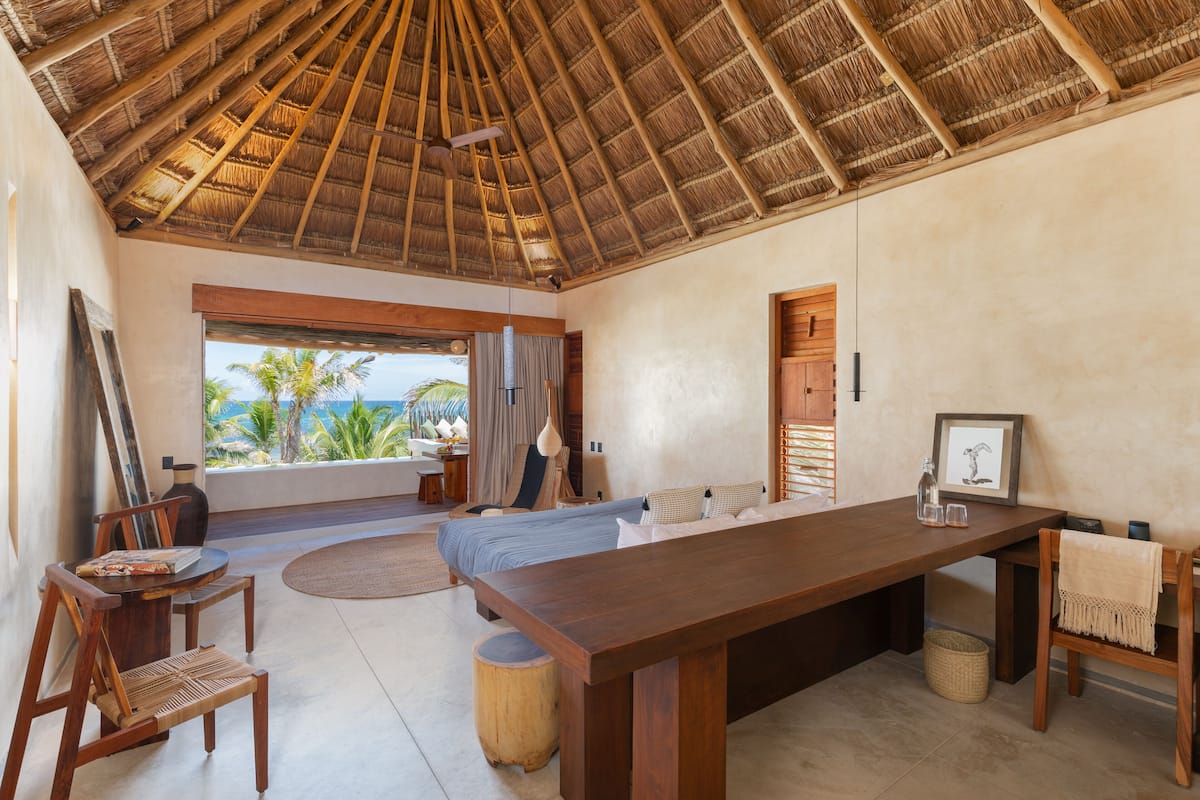 Una habitación amplia con una gran mesa de madera, una cama cómoda y vistas a palmeras y al océano.