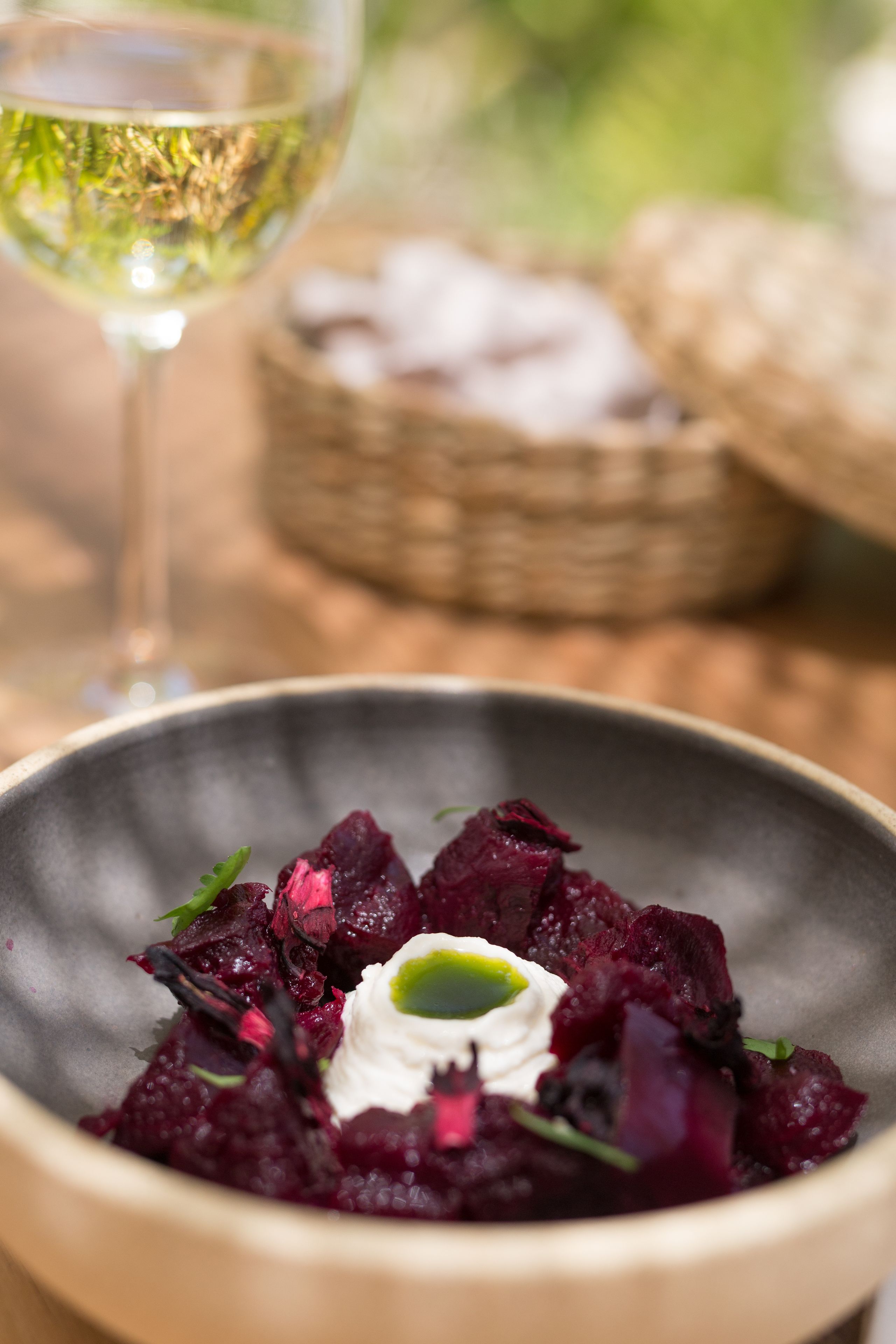 A bowl of beetroot salad with a white dollop of cream and a green leaf garnish, accompanied by a glass of white wine.