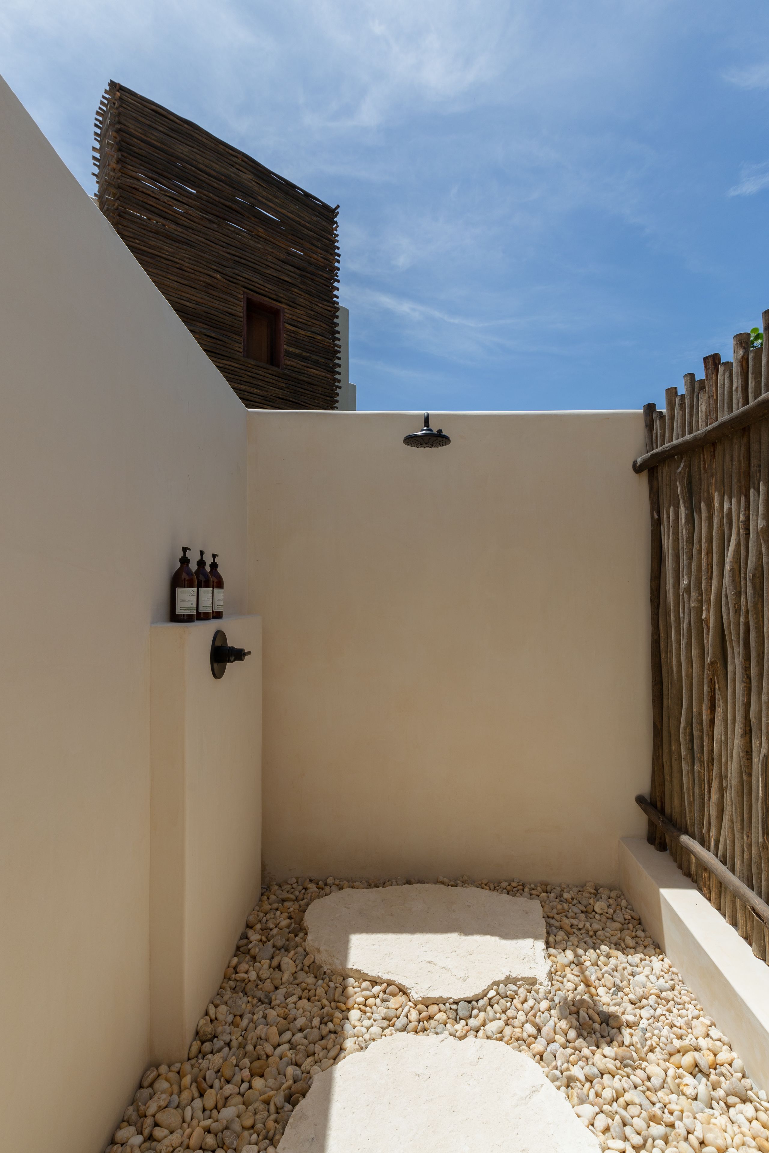 Un pequeño espacio exterior para ducha, con suelo de piedra, valla de madera y ducha de pared.