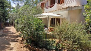 A two-story building with a patio area, surrounded by various plants and trees.