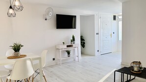 A modern, minimalist living room with a dining area, a flat-screen TV mounted on the wall, and a white console table with plants. - SEA VIEW APT, BEACHFRONT, PARKING, AA/CC, WIFI, LARGE TERRACE (Salou)