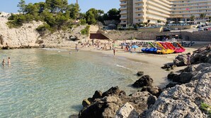 A beach with clear waters, rocky shore, and a multi-story hotel in the background. - SEA VIEW APT, BEACHFRONT, PARKING, AA/CC, WIFI, LARGE TERRACE (Salou)