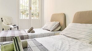 Habitació amb dos llits, una cadira i una finestra que dona a zona verda.