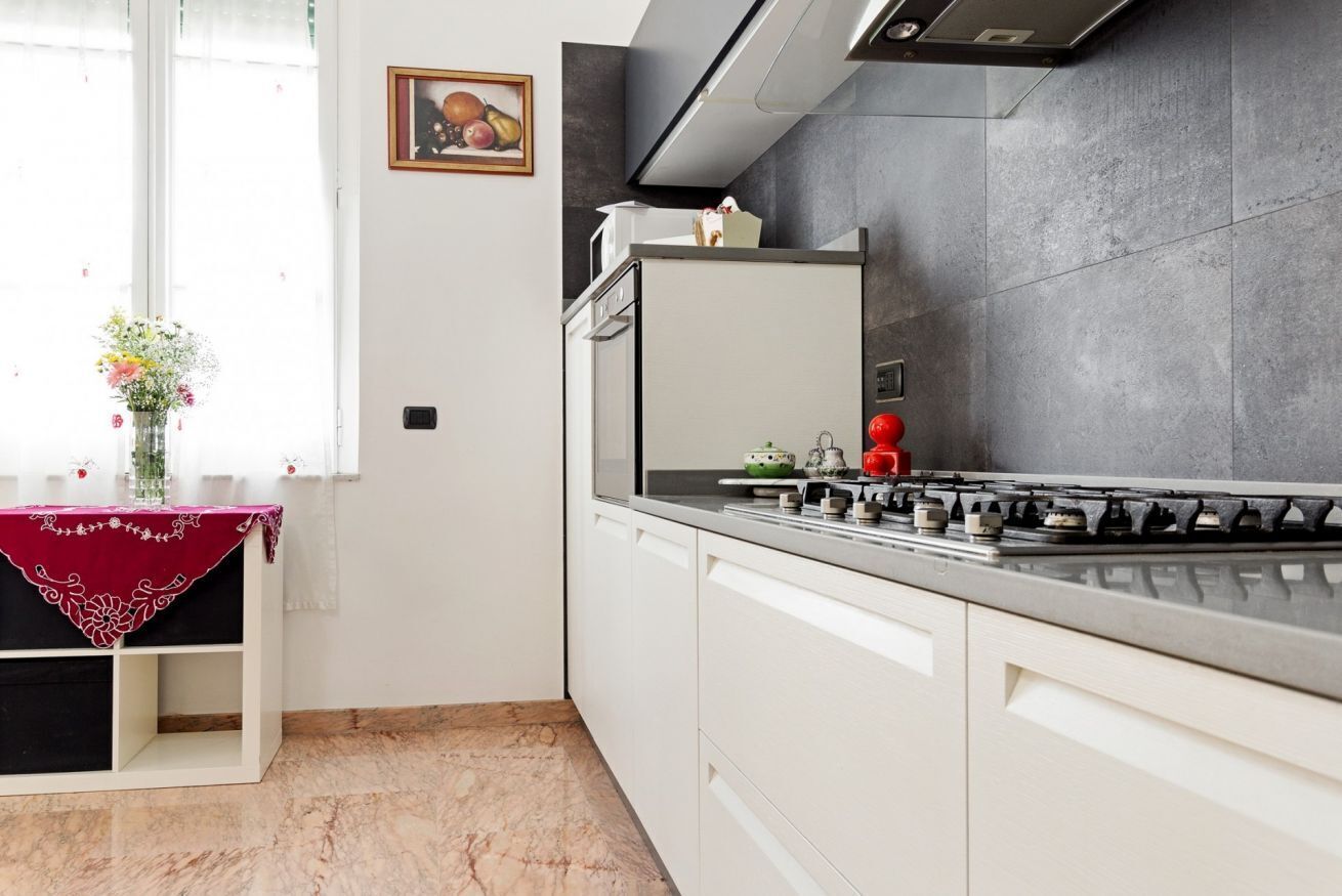Une cuisine moderne avec une cuisinière à gaz, des armoires blanches et un sol en marbre.