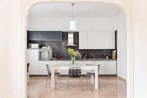 Une cuisine moderne avec des armoires blanches, un four en acier inoxydable, un four à micro-ondes et une table à manger avec des chaises.