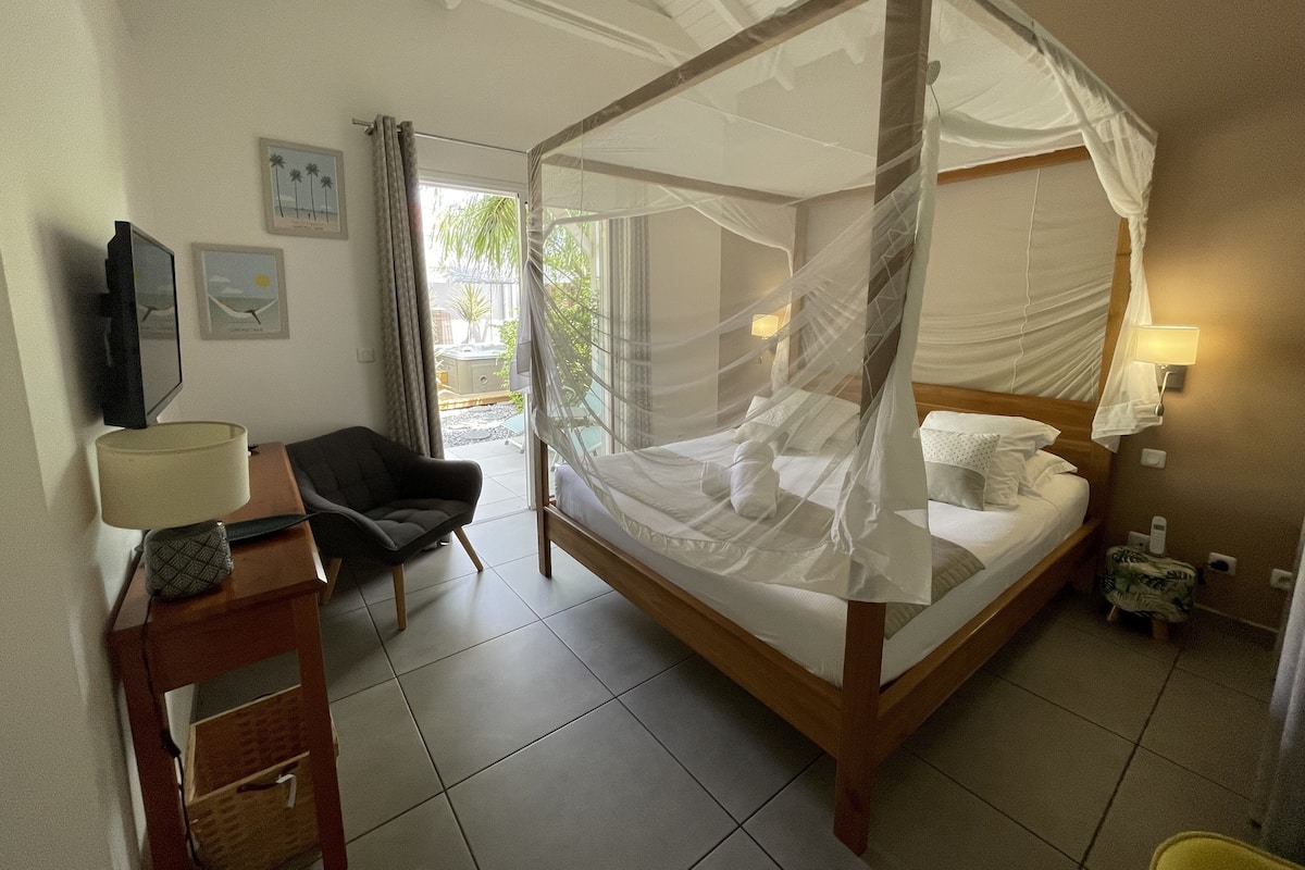 A bedroom with a four-poster bed, a TV, a desk with a lamp, and a chair.