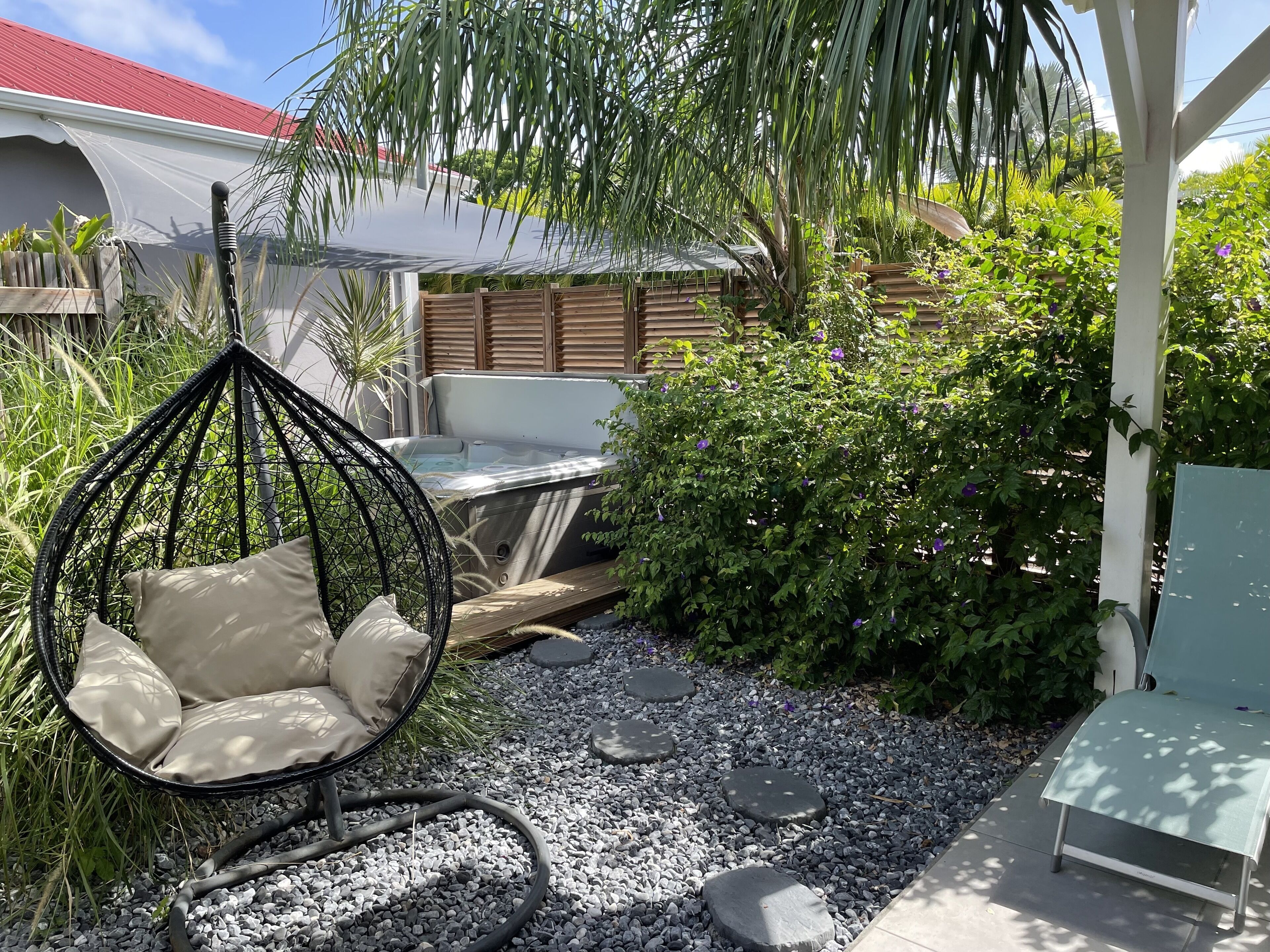 A garden with a hanging chair, a hot tub, and a variety of plants.