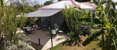 Un patio con mesa y sillas, rodeado de plantas y un paraguas grande.