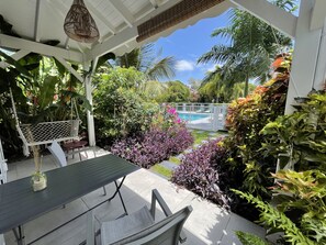 Un espacio al aire libre cubierto con una mesa y sillas, rodeado de exuberante vegetación tropical y vista a una piscina.