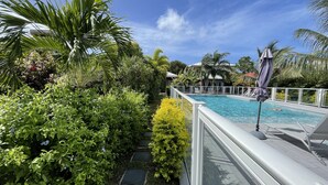 A pool area with a clear view of the pool, surrounded by lush greenery and a white deck. - Le Cocotel (Saint-François)