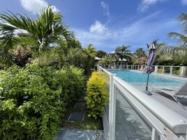 A pool area with a clear view of the pool, surrounded by lush greenery and a white deck.