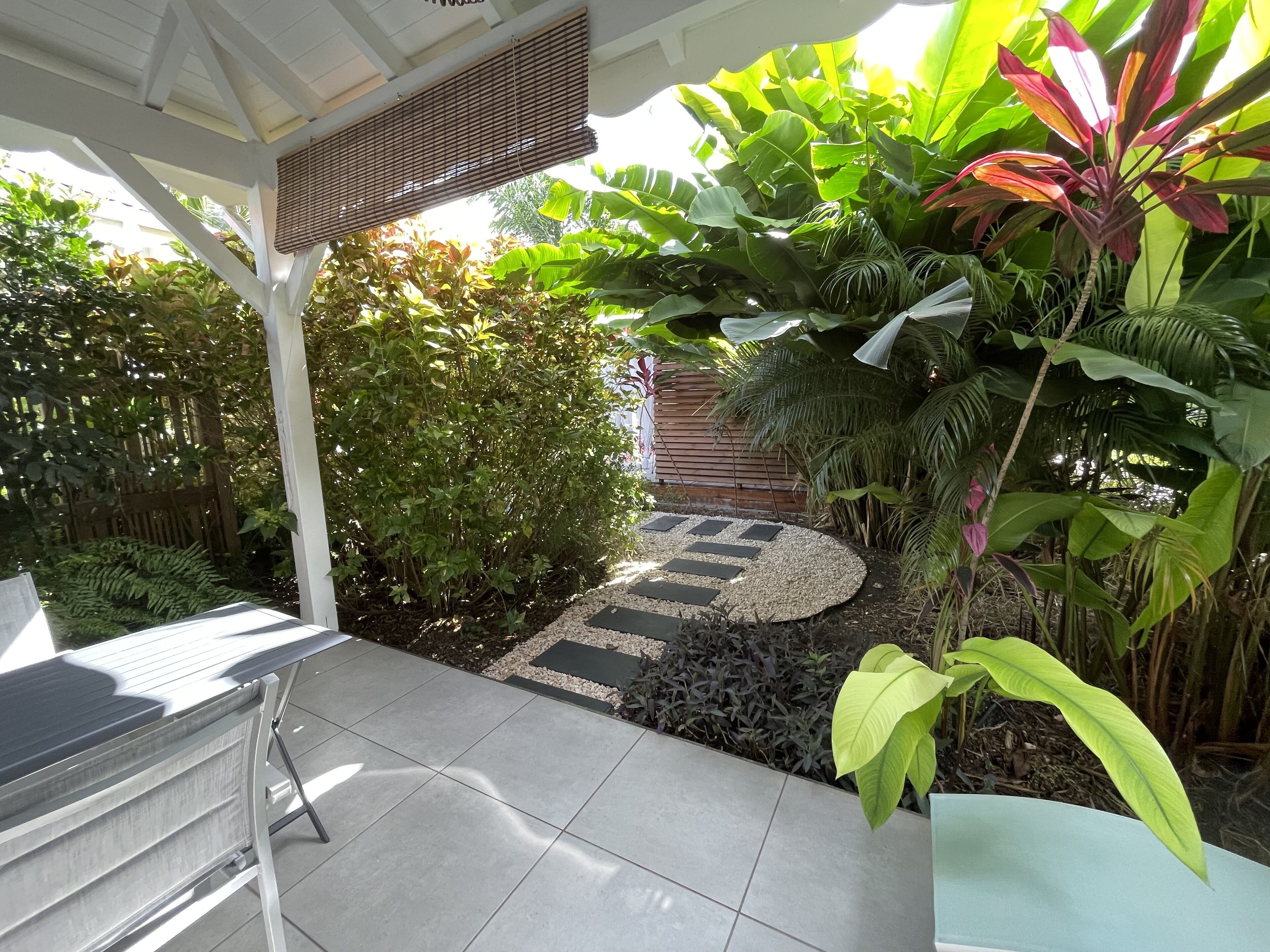 Un patio con suelo de baldosas, una pérgola con techo de mimbre y abundante vegetación.