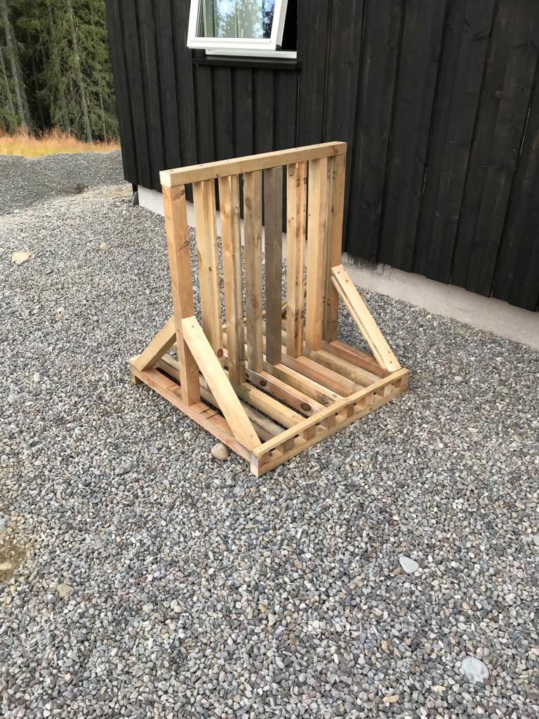 A wooden pallet chair outdoors on gravel, with a black building and a window in the background.