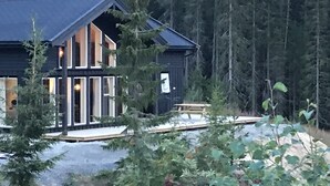 Une cabane dotée d’une grande véranda, de nombreuses fenêtres et d’une terrasse.