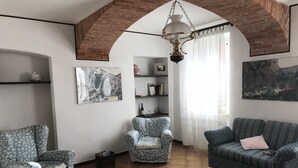 A living room with a patterned armchair, a sofa, a large rug, and a hanging lamp. - Bed & Roses "Gege"   (La Morra)