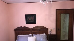 A bedroom with a wooden headboard, a bed with grey bedding, a white pillow, a nightstand with a lamp, and a door with a frosted glass panel. - Bed & Roses "Gege"   (La Morra)