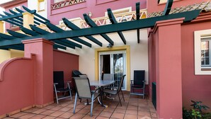 Un espace patio aménagé avec une table et des chaises, une pergola et une porte donnant sur l’intérieur.
