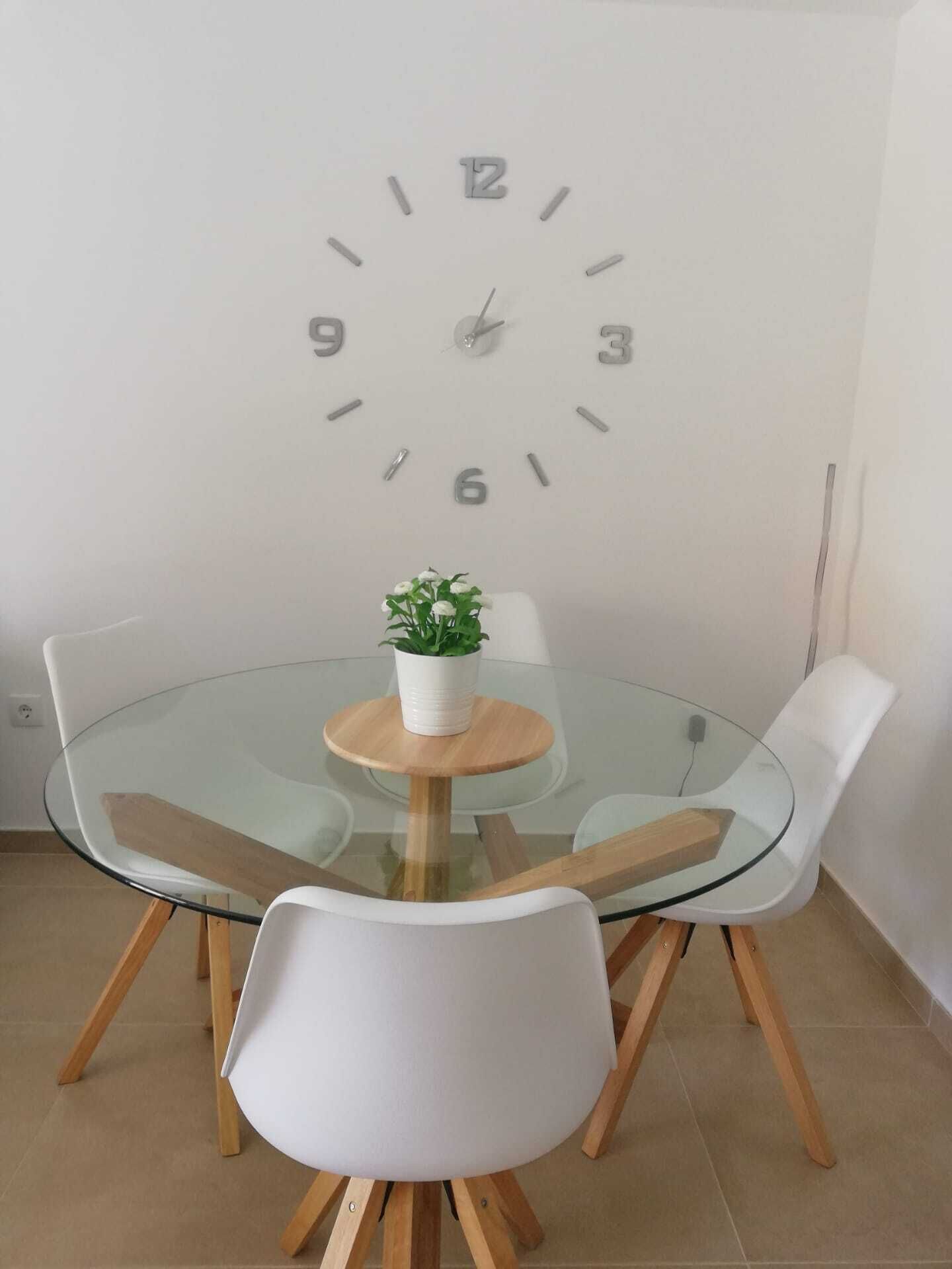 Ein moderner Essbereich mit einem Glastisch, weißen Stühlen und einer Wanduhr.