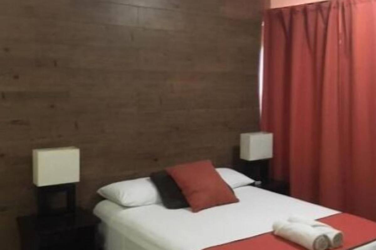 A hotel room with a bed, two bedside tables with lamps, a ceiling fan, and a red curtain.