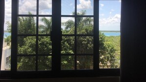 A window with a view of a tropical landscape, including trees and a body of water. - Hotel Tuparenda Bacalar (Bacalar)