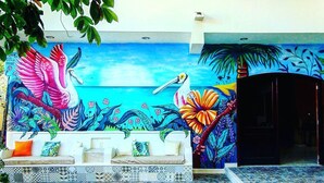 A colorful mural with a bird, a flower, and a sea scene on a building facade. - Hotel Tuparenda Bacalar (Bacalar)