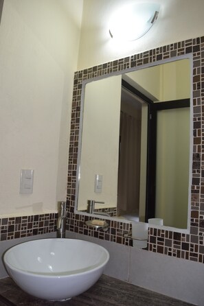 Une salle de bain avec un lavabo blanc, un miroir et un mur recouvert de carreaux.