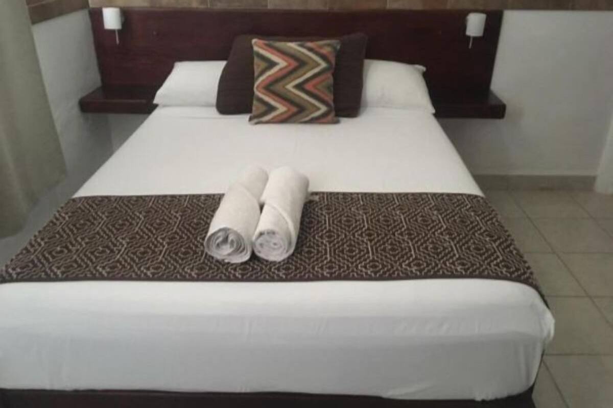 A neatly made bed with a patterned bedspread and two rolled towels.