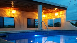 A swimming pool with a metal ladder, surrounded by a building with large windows and warm lighting. - Hotel Tuparenda Bacalar (Bacalar)
