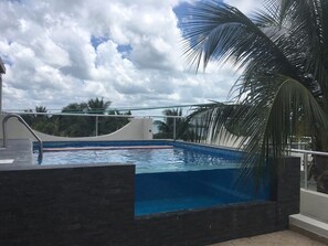 Une piscine dotée d’un bassin aux eaux d’un bleu limpide, entourée d’une terrasse carrelée de couleur sombre et d’un garde-corps en verre.