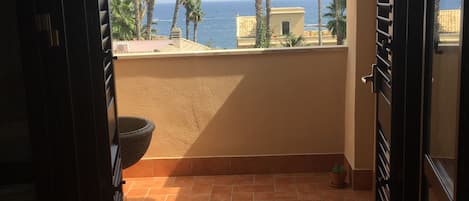 Un balcón abierto con vista al mar y palmeras.
