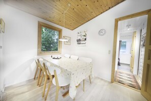 Un comedor con techo de madera, paredes blancas, una ventana, un reloj y una puerta que da a otra habitación.