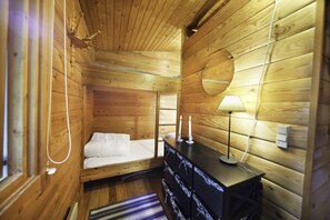 Un dormitorio de cabaña de madera con cama, cómoda y lámpara.