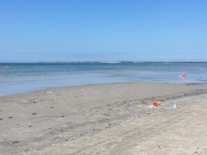 Una playa con cielo despejado, agua tranquila y una costa distante.