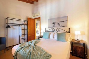 A bedroom with a bed, a nightstand, a wall-mounted shelf, a door, and a painting.