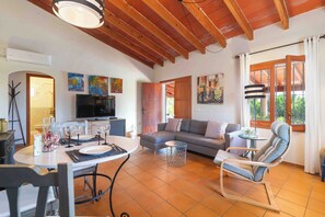 A living room with a sofa, a dining table with chairs, a TV, and artwork on the walls.