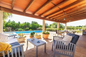 A covered outdoor seating area with a pool, chairs, and tables.