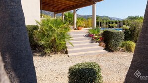 Un espacio al aire libre techado con escaleras que conducen a una piscina, rodeado de plantas variadas y un paisaje montañoso.