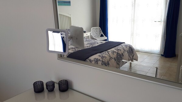 Un dormitorio con cama, una silla, un escritorio y un espejo.