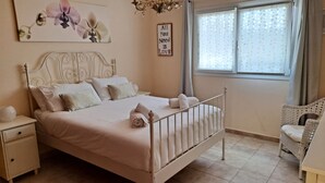 A bedroom with a bed, nightstands, a chair, a window with curtains, and a wall with a floral painting and a motivational quote. - Villa Essence - with A/C, heated private pool, hottub, gardens & stunning views! (Tias)